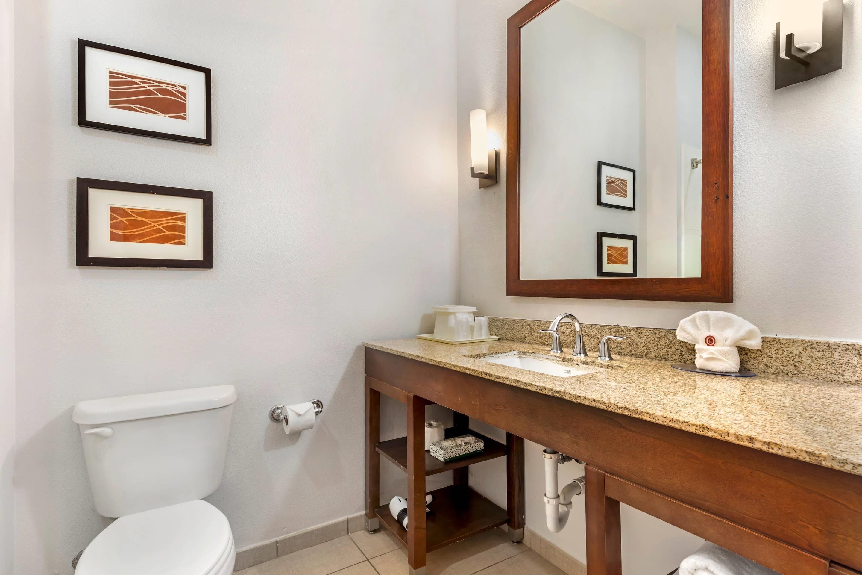 A bathroom with a white toilet, a wooden vanity with a sink, and two framed artworks on the wall.