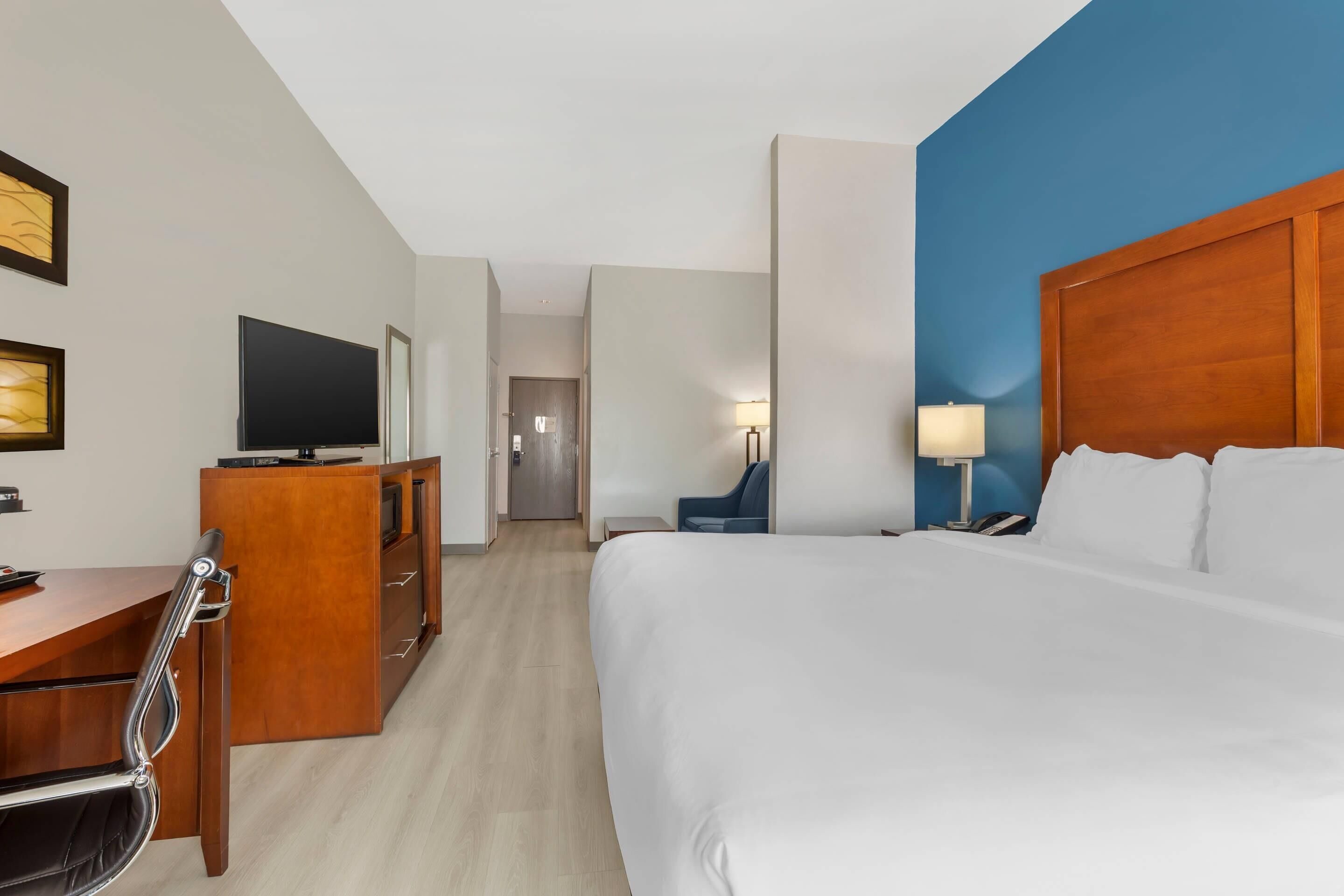 A hotel room with a large bed, a desk with a chair, a TV, and a lamp.