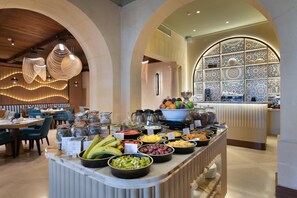 En buffet med forskellige retter, et siddeområde med borde og stole, og en dekorativ væg med et mønster.