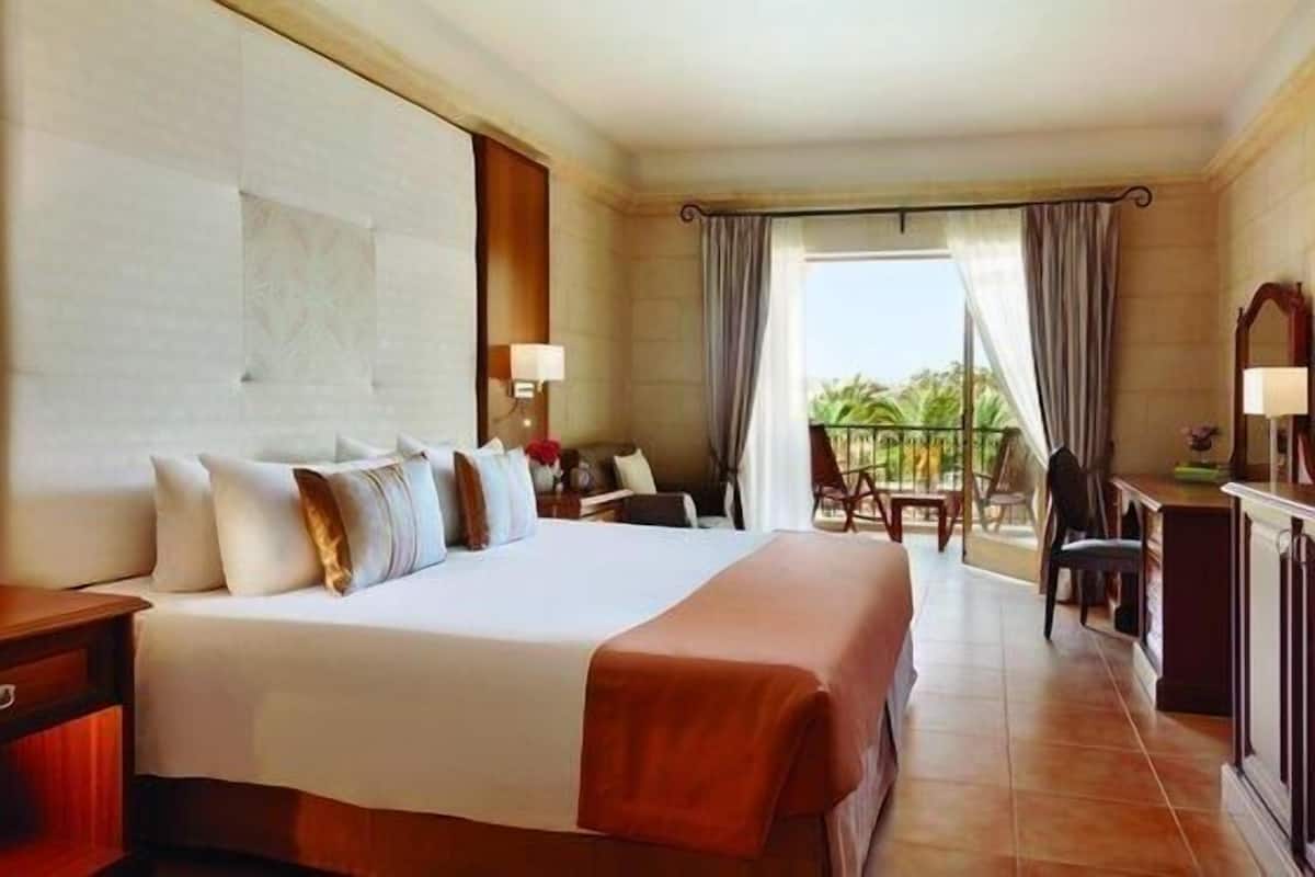 Ein Hotelzimmer mit einem großen Bett, einem Schreibtisch, einem Stuhl, einem Balkon mit Blick und einem Vorhangfenster.