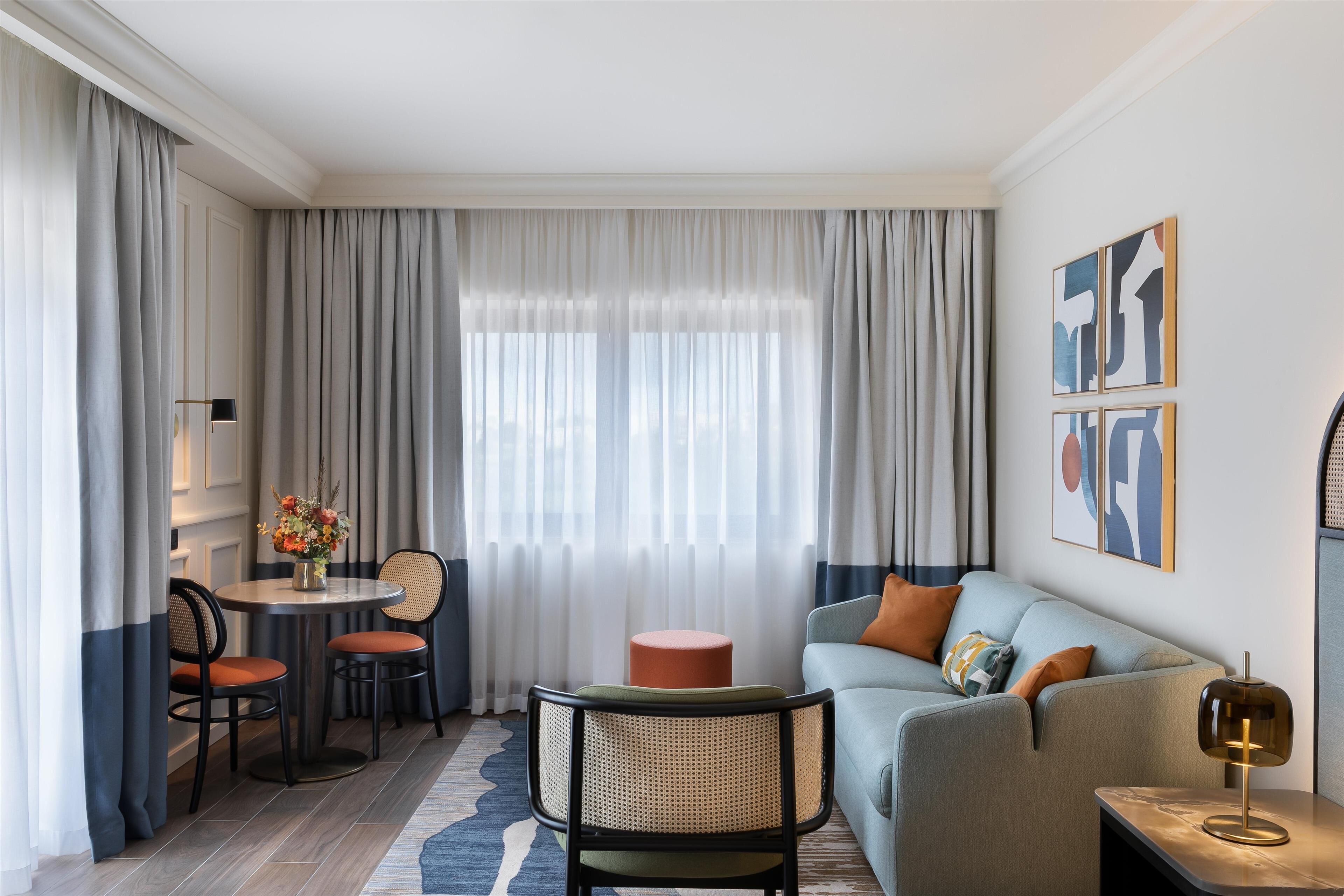 Un salon moderne avec un canapé, des fauteuils, une petite table sur laquelle est posé un vase de fleurs et une lampe.