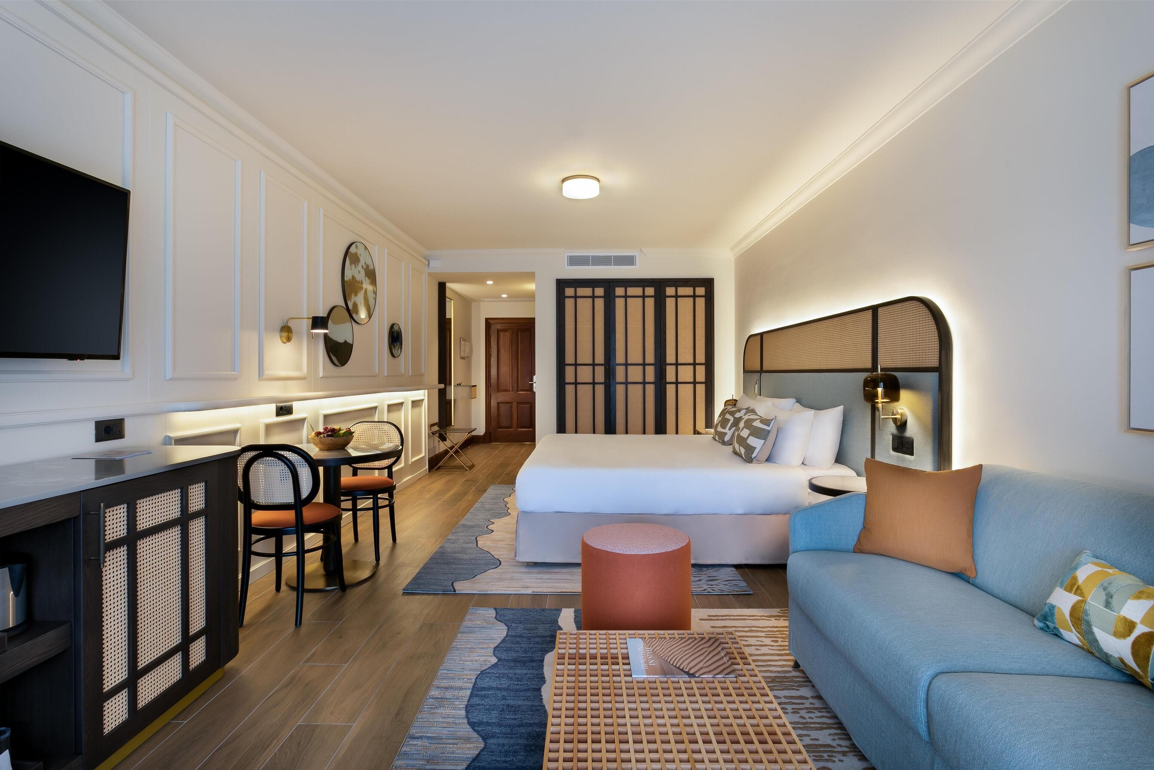 A modern hotel room with a bed, a sofa, a desk, and a TV.