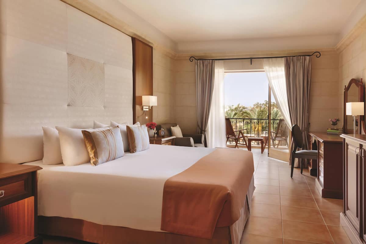 Une chambre d’hôtel avec un grand lit, un bureau, une chaise, un balcon avec vue et une fenêtre avec des rideaux.