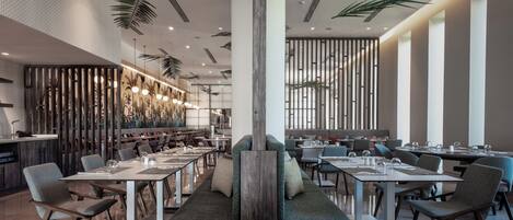 A modern restaurant with high ceilings, pendant lighting, and a central seating area.