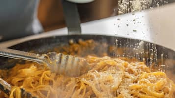 A person cooking pasta in a pan, with a bowl of grated cheese nearby.