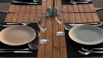 Une table de salle à manger en bois, dressée avec des assiettes, des couverts et des verres, donnant sur une étendue d’eau.