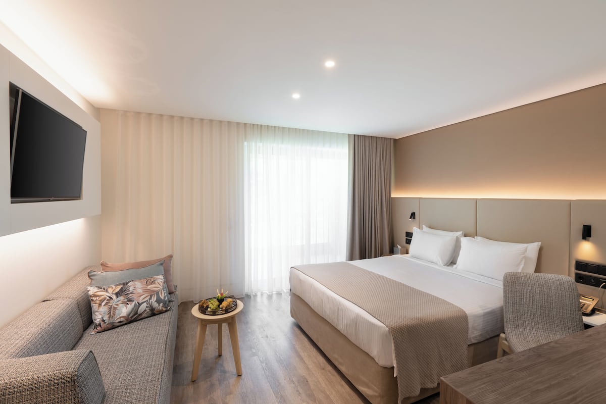 Une chambre d’hôtel avec un lit, un canapé, une petite table avec des fruits et un téléviseur fixé au mur.