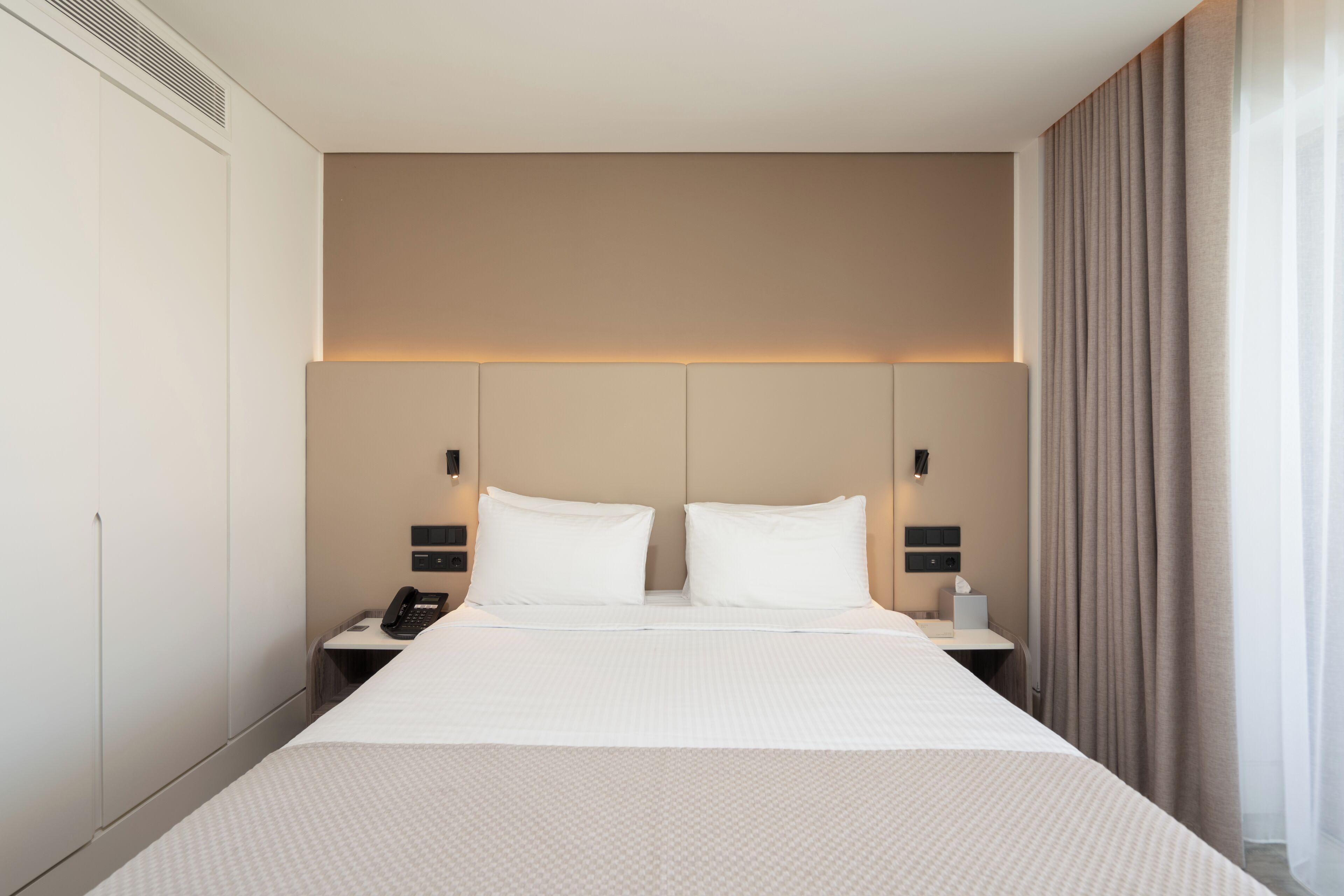 A hotel room with a large bed, bedside tables, a phone, and a lamp.