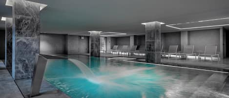 A modern indoor pool with marble columns, lounge chairs, and a clear water feature.