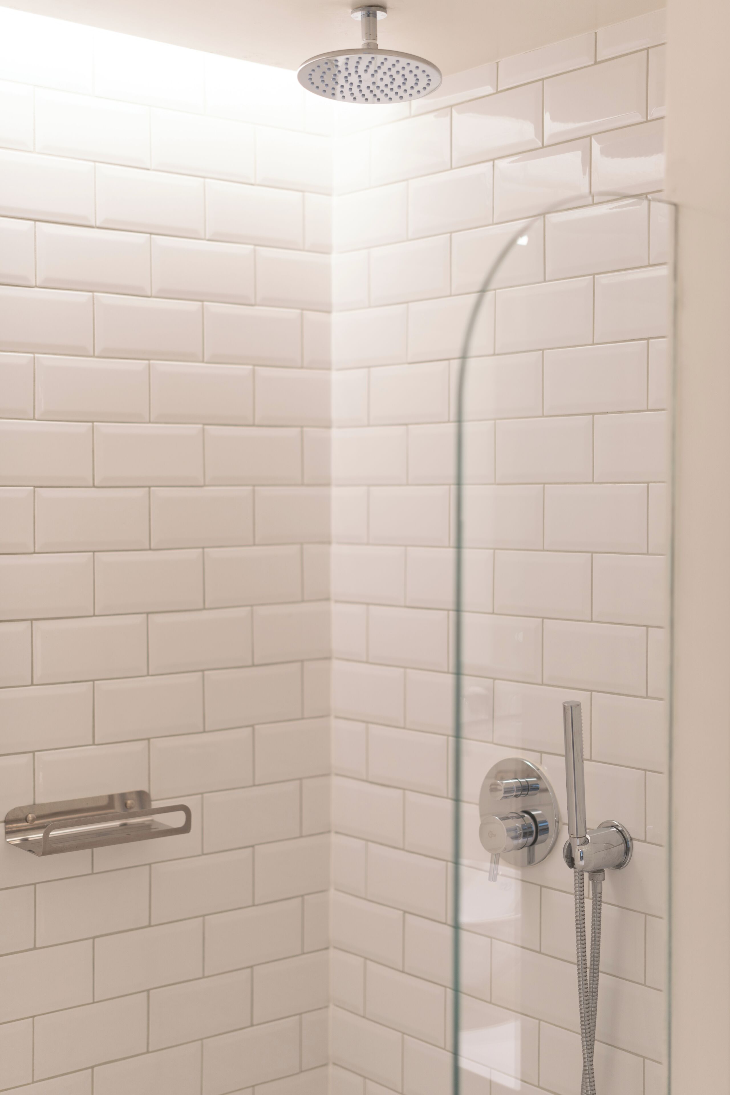A corner shower with white tiles, a glass door, and a handheld showerhead.