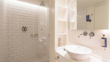 A bathroom with a white-tiled shower, a sink with a large basin, and a mirror above the sink.