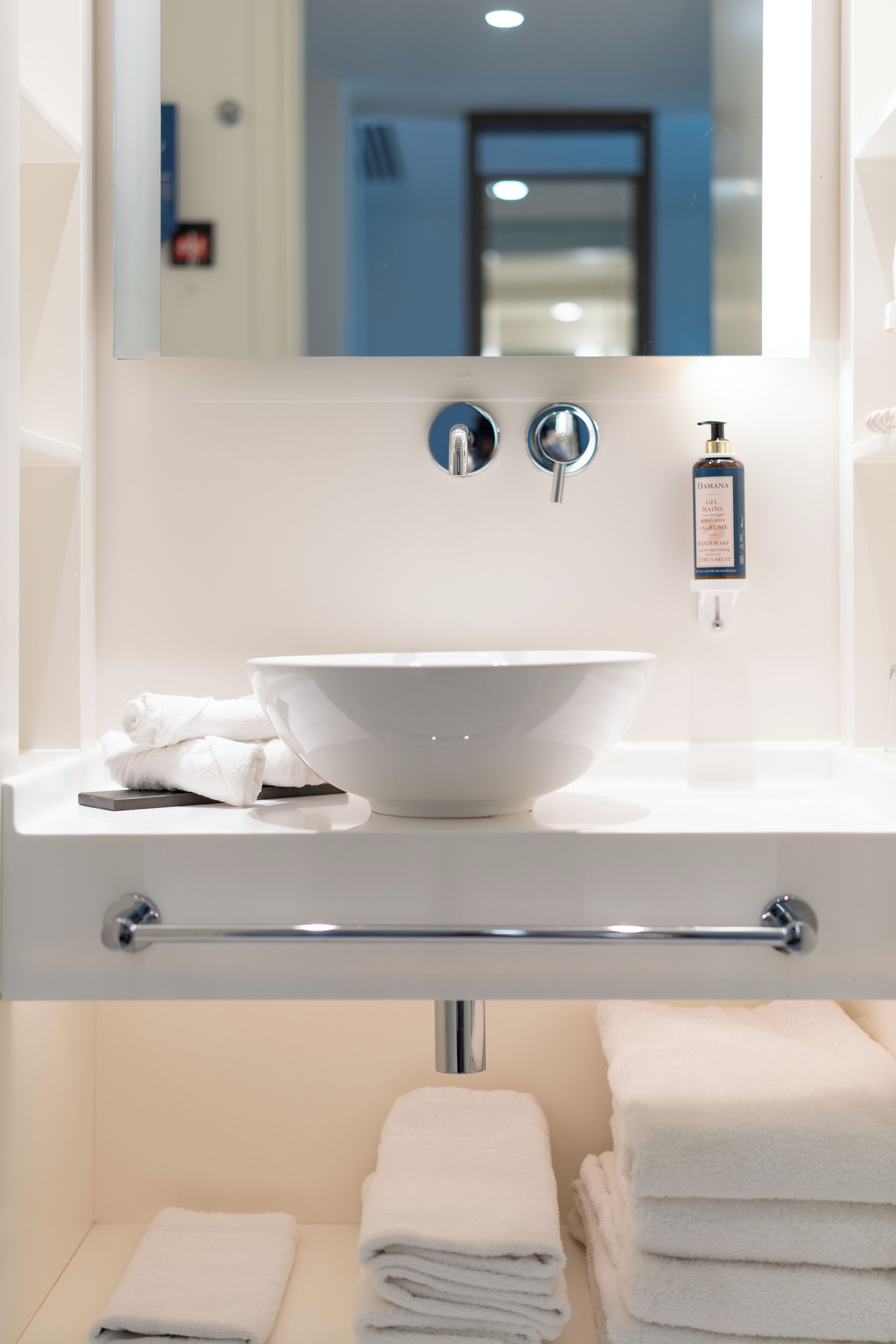 Un baño moderno con un lavamanos blanco, un espejo grande y un perchero para toallas.