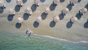 Une vue aérienne d’une plage avec une eau cristalline, des parasols et des chaises longues.