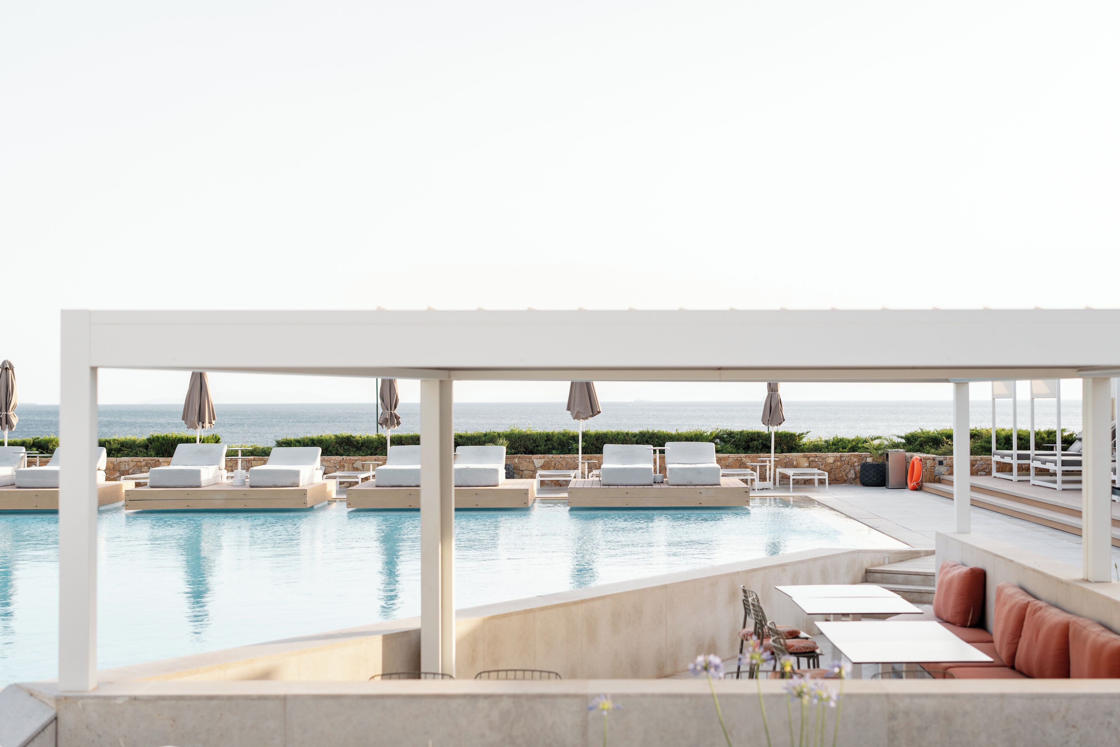 Un área junto a la piscina con sillones de descanso, sombrillas y una zona de estar con cojines.