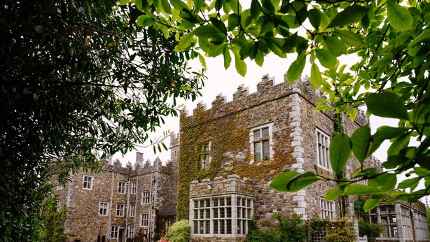 A historic stone building with ivy-covered walls, a central courtyard with a bench, and a view of the surrounding greenery.
