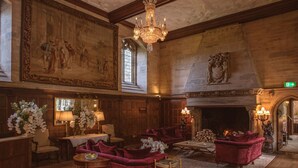 A grand room with a fireplace, red velvet sofas, and a large mural on the wall.