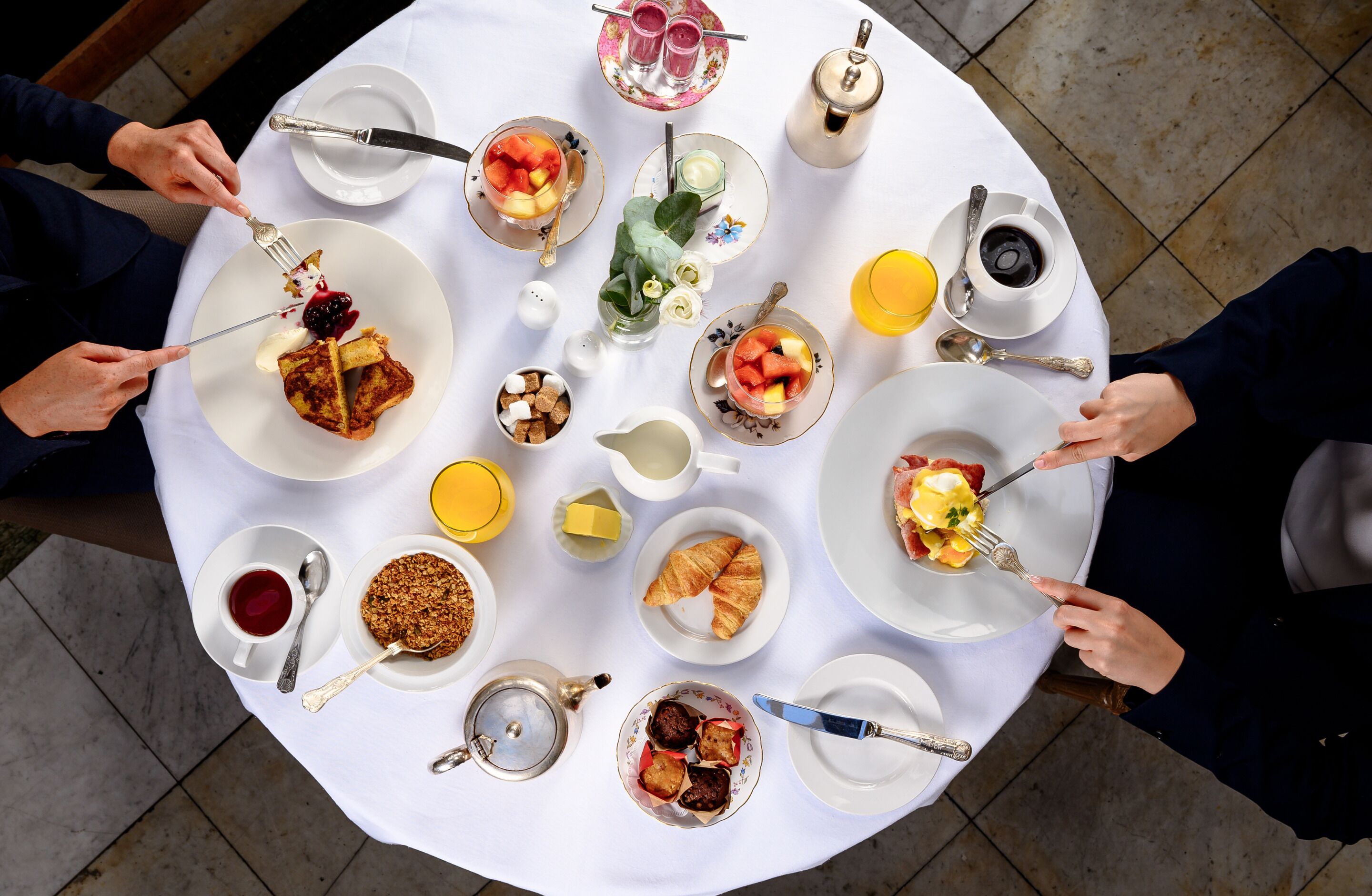 A round table with various breakfast items including croissants, fruit, and beverages.