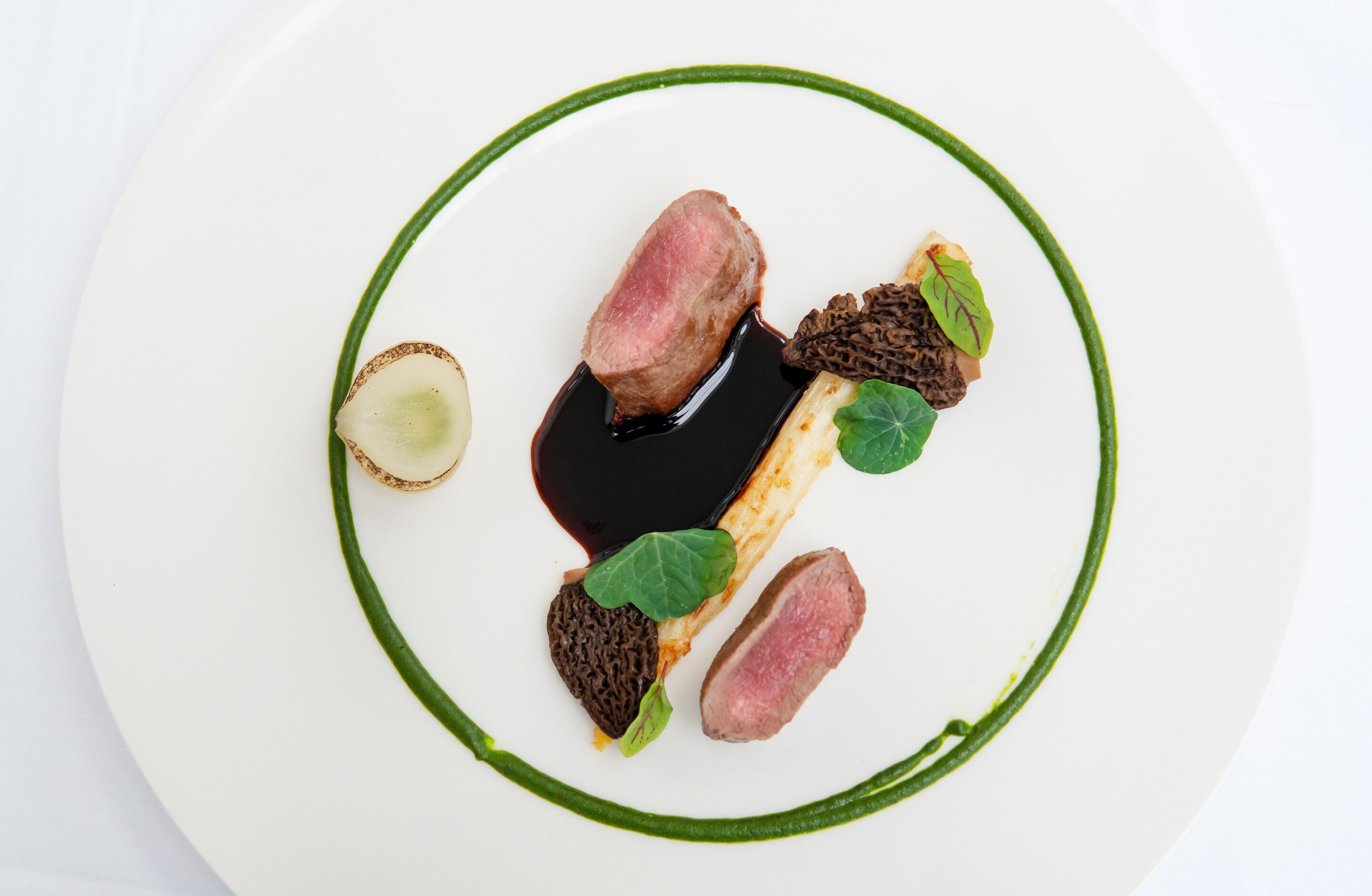 A white plate with a green rim, containing a piece of meat, a slice of vegetable, and some dark brown mushrooms.