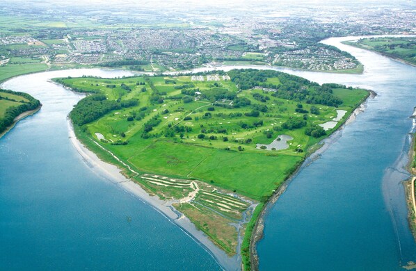 Vista aérea de una isla costera con campos verdes, un campo de golf y un río.