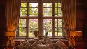 A room with a large window, a sofa with floral cushions, and two lamps on side tables.