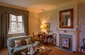 A traditional living room with a blue sofa, a fireplace, a desk with a lamp, and a large mirror on the wall. - Waterford Castle (Waterford)