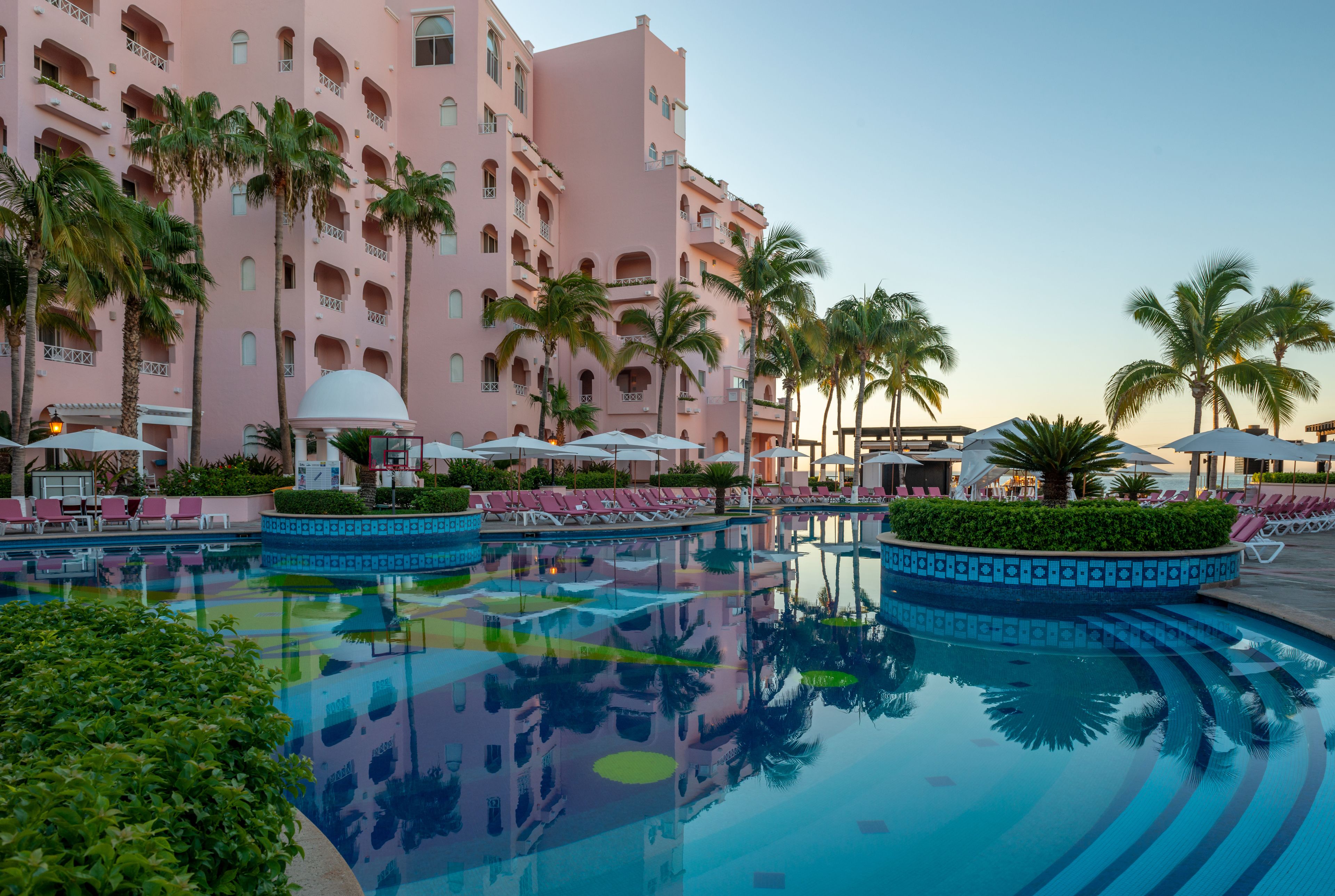 A hotel with a pool, palm trees, and lounge chairs.