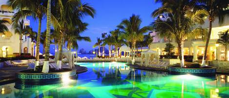 A pool area with palm trees and lounge chairs, surrounded by buildings with white facades and balconies.