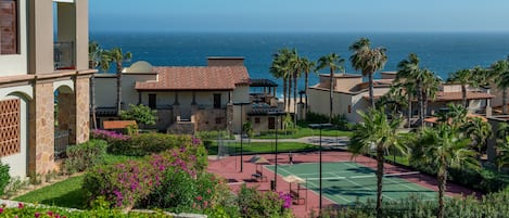 A resort with a tennis court, palm trees, and ocean views.