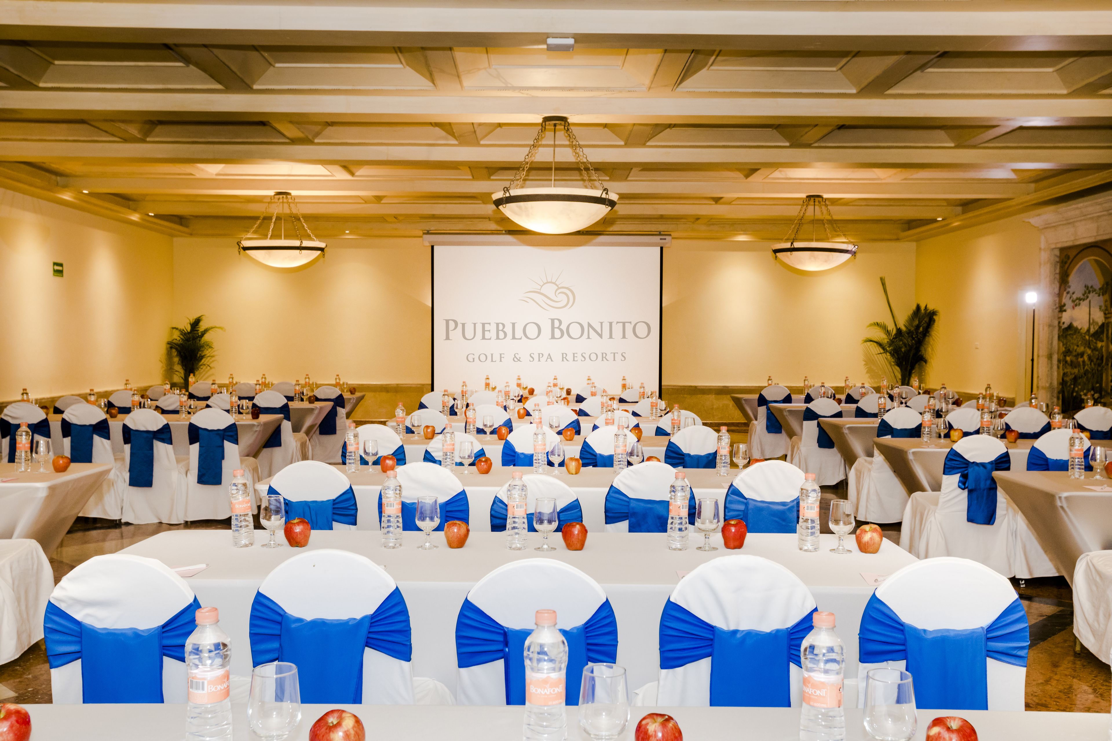 Ein Konferenzraum im Pueblo Bonito Golf & Spa Resorts mit für ein Meeting gedeckten Tischen, inklusive blauer Bänder und Wasserflaschen.