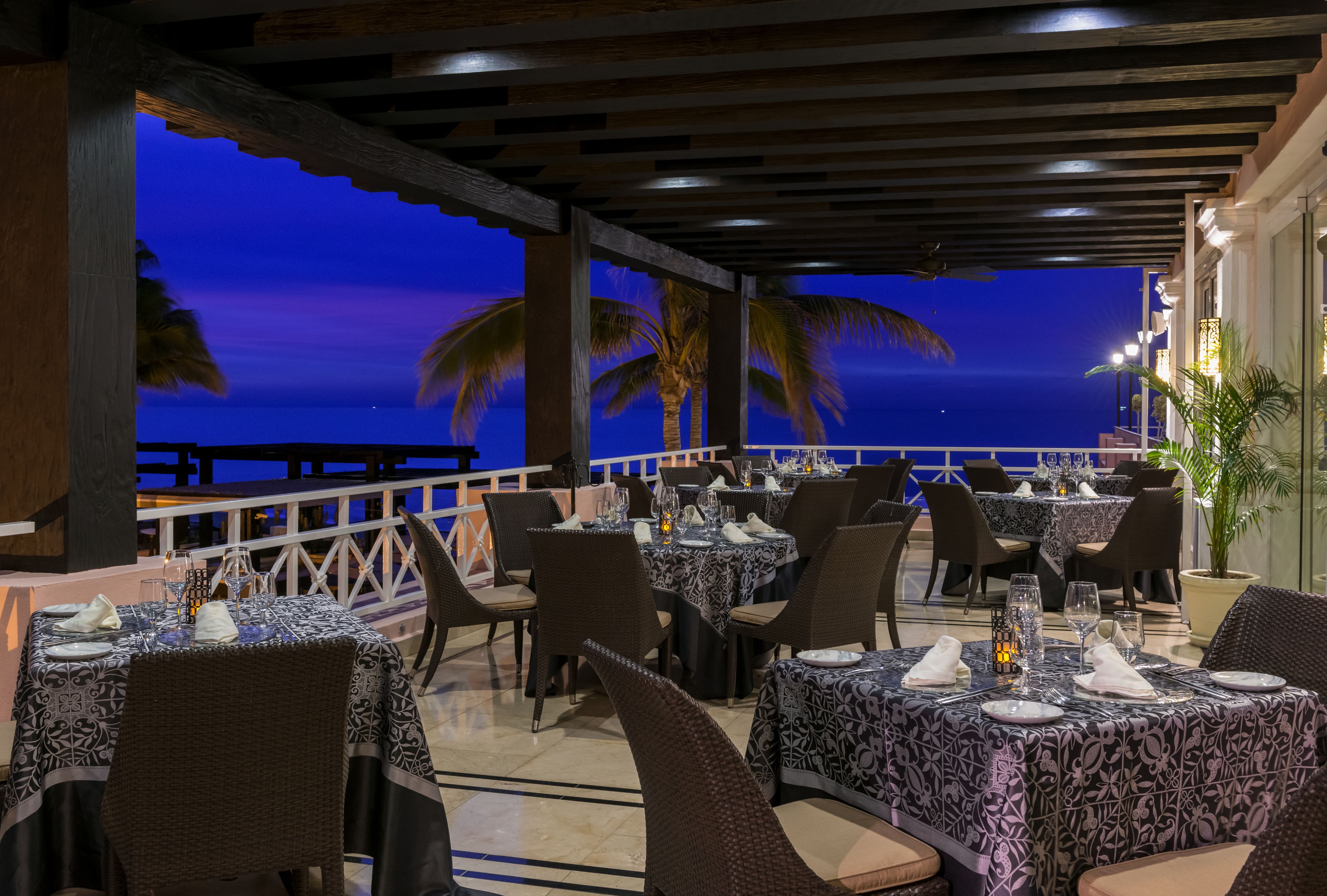 Un restaurante con mesas dispuestas para comer, con vistas a un cuerpo de agua al anochecer.