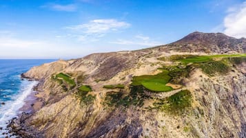 A rugged coastline with a mountain, a golf course, and a small building.