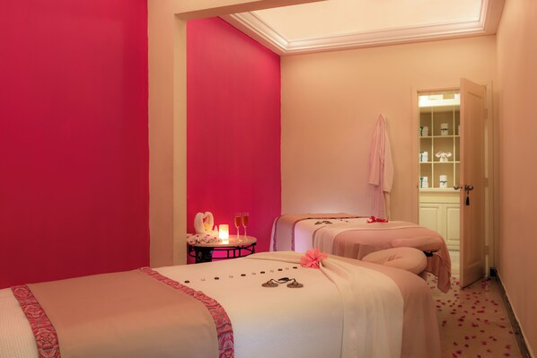 A room with two beds, a small table with a candle and two glasses, and a door leading to a bathroom. - Pueblo Bonito Rose Resort and Spa - All Inclusive (Cabo San Lucas)