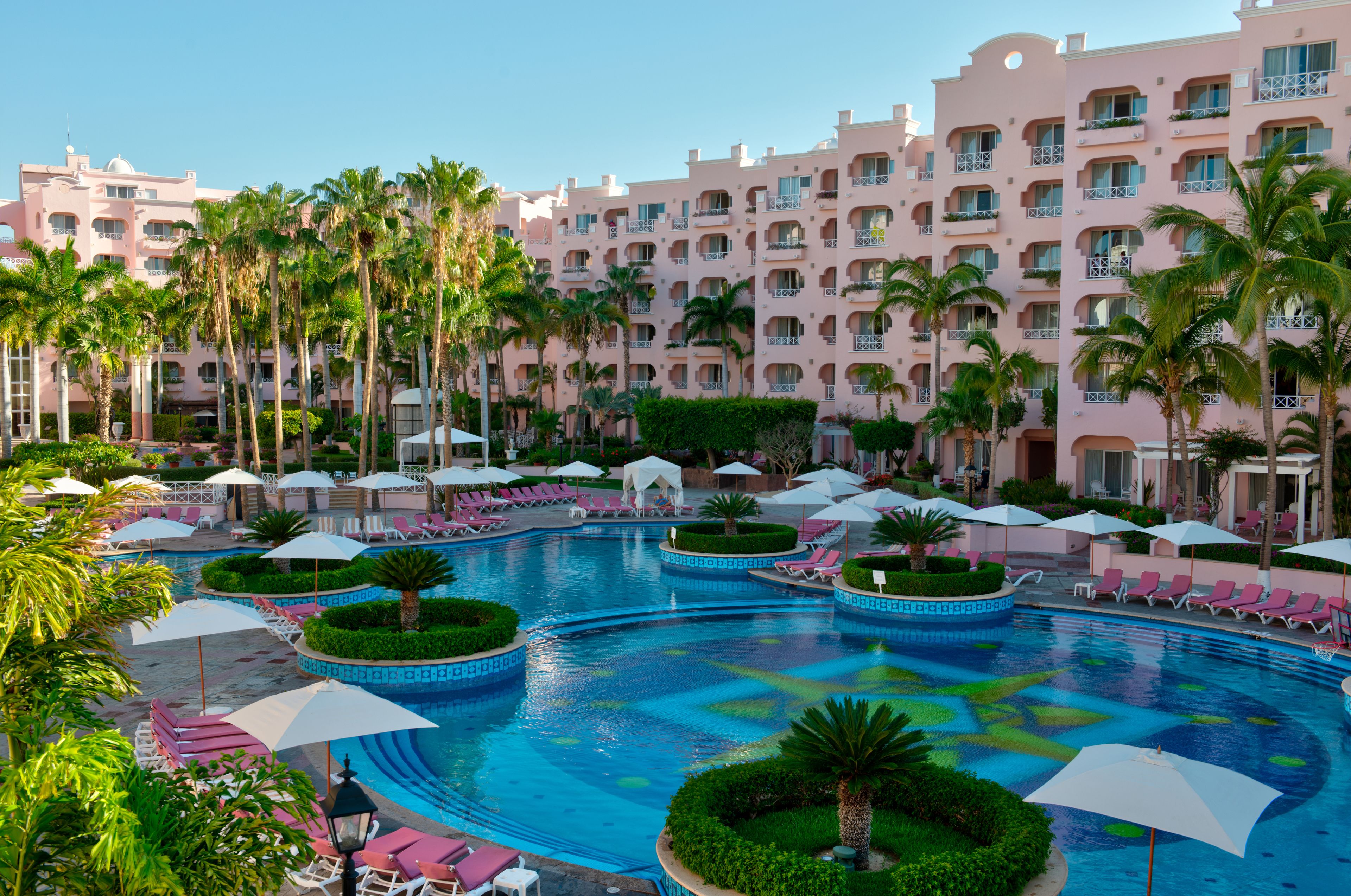 A resort with a large swimming pool surrounded by palm trees and lounge chairs.
