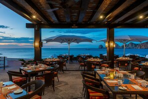 An outdoor dining area with tables and chairs, umbrellas, and a view of the sea. - Pueblo Bonito Rose Resort and Spa - All Inclusive (Cabo San Lucas)