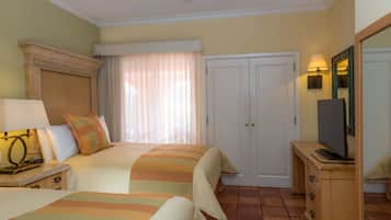 A hotel room with two beds, a television on a wooden dresser, a mirror, and a door with a light above it.