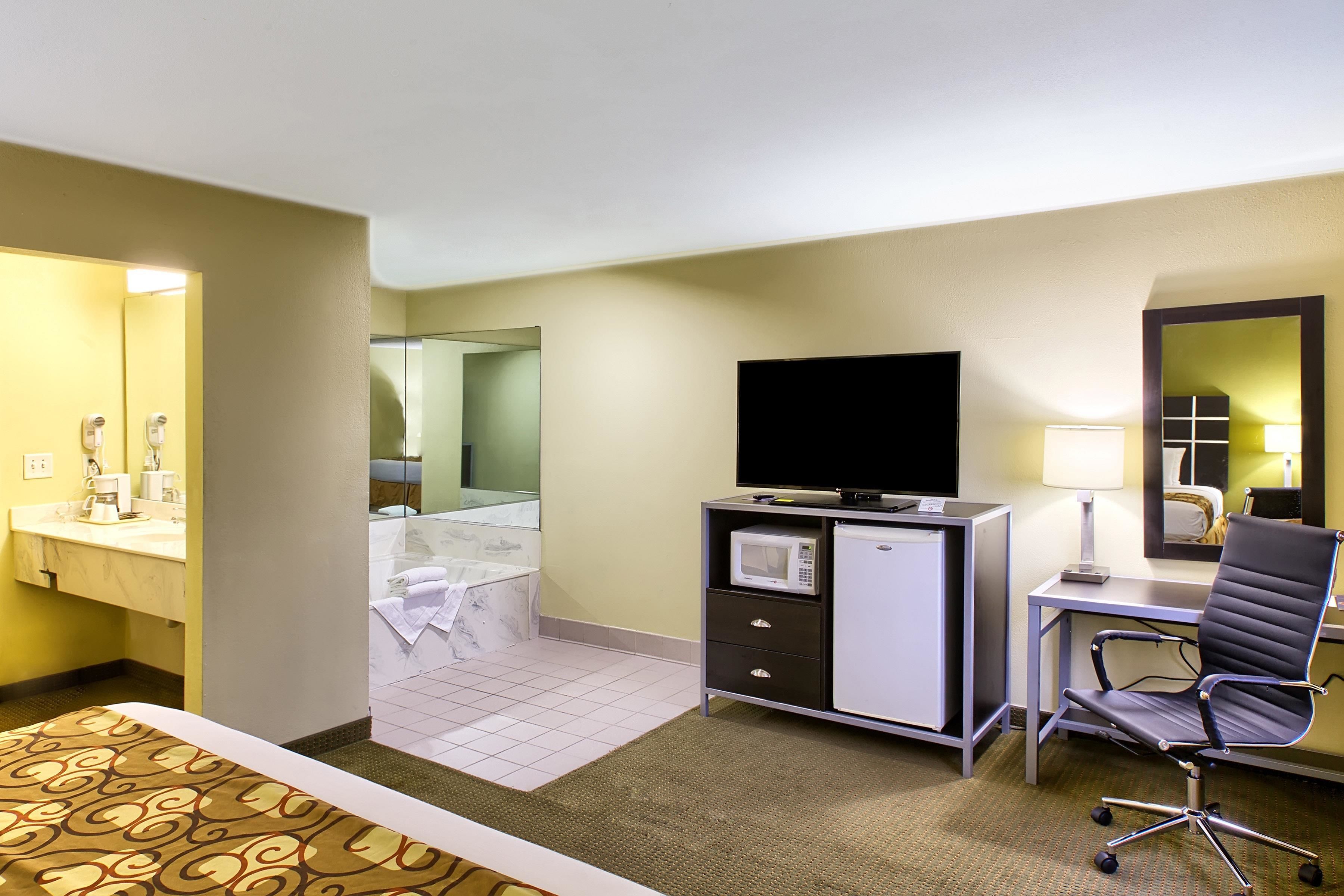 Une chambre d’hôtel comprenant un lit, un bureau avec une chaise, une télévision, un four à micro-ondes et une salle de bain avec un miroir.