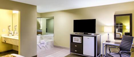 Une chambre d’hôtel comprenant un lit, un bureau avec une chaise, une télévision, un four à micro-ondes et une salle de bain avec un miroir.