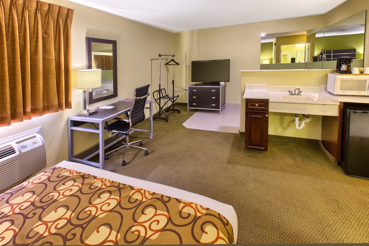 A hotel room with a bed, desk, chair, television, dresser, and a bathroom with a sink and mirror.