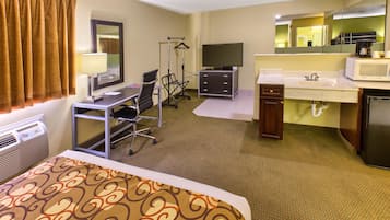 A hotel room with a bed, desk, chair, television, dresser, and a bathroom with a sink and mirror.