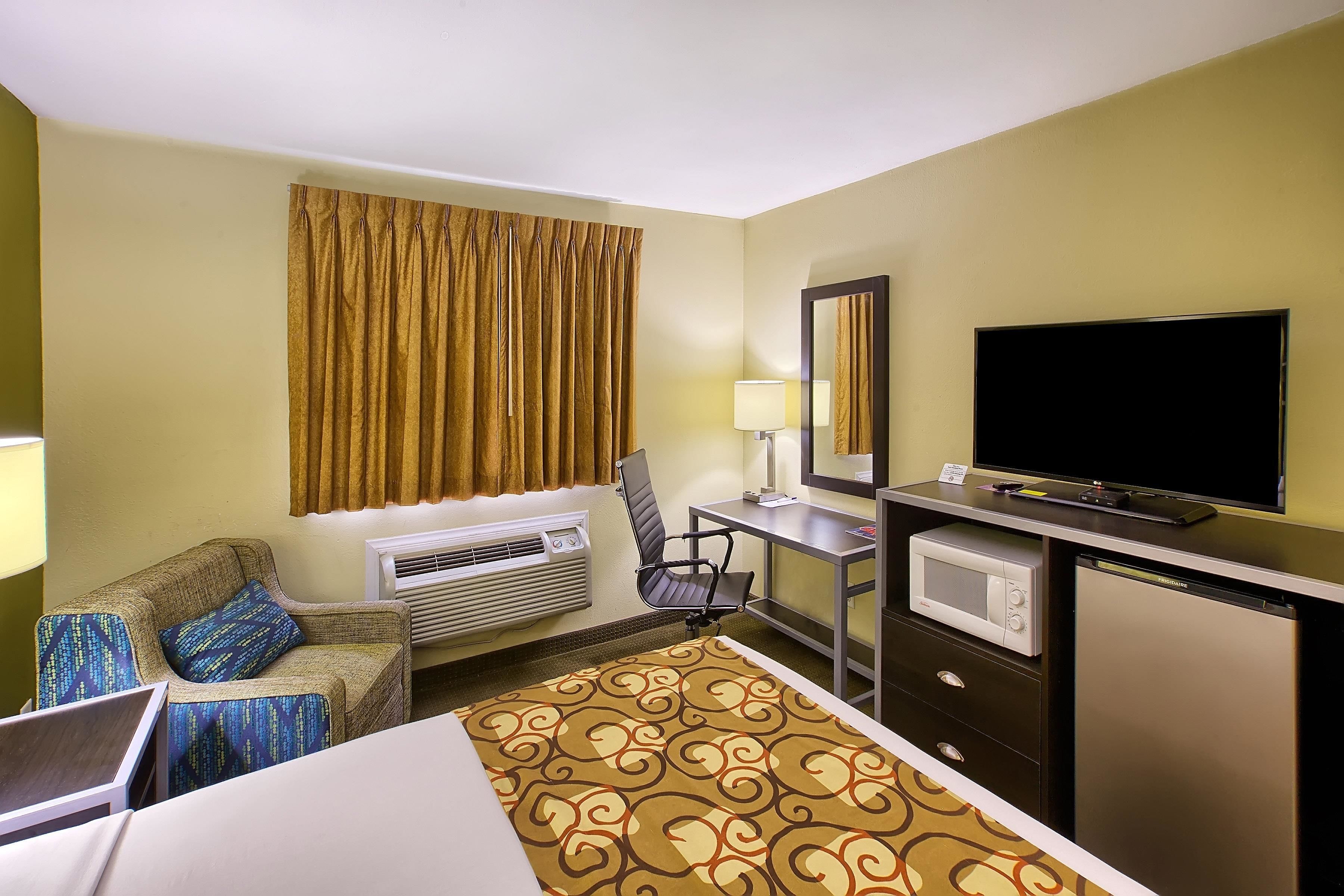 A hotel room with a bed, a desk with a computer, a television, a microwave, and an air conditioning unit.