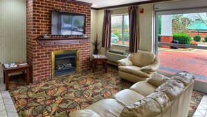 A living room with a brick fireplace, a flat-screen TV, a beige sofa, and a patterned carpet. - Country Hearth Inn Knightdale Raleigh (Knightdale)