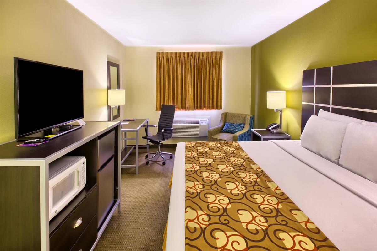 A hotel room with a bed, desk, chair, television, and a microwave.