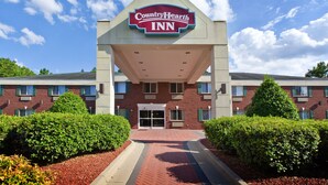 A CountryHearth Inn with a prominent sign, brick exterior, and a paved entrance. - Country Hearth Inn Knightdale Raleigh (Knightdale)