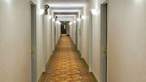 A long, narrow hotel corridor with patterned carpet, light-colored walls, and wall-mounted light fixtures. - Country Hearth Inn Knightdale Raleigh (Knightdale)