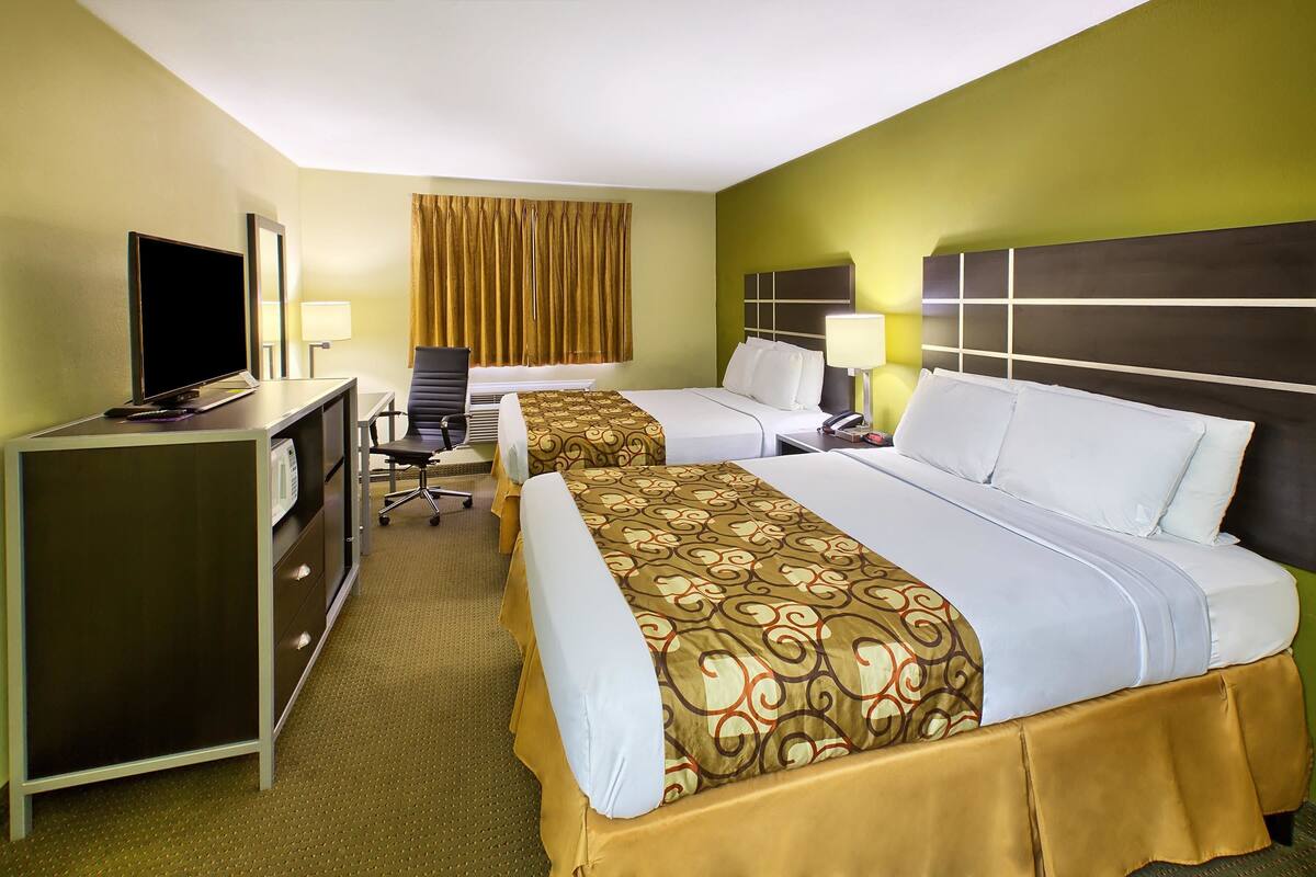 A hotel room with two beds, a desk with a TV, and a chair.