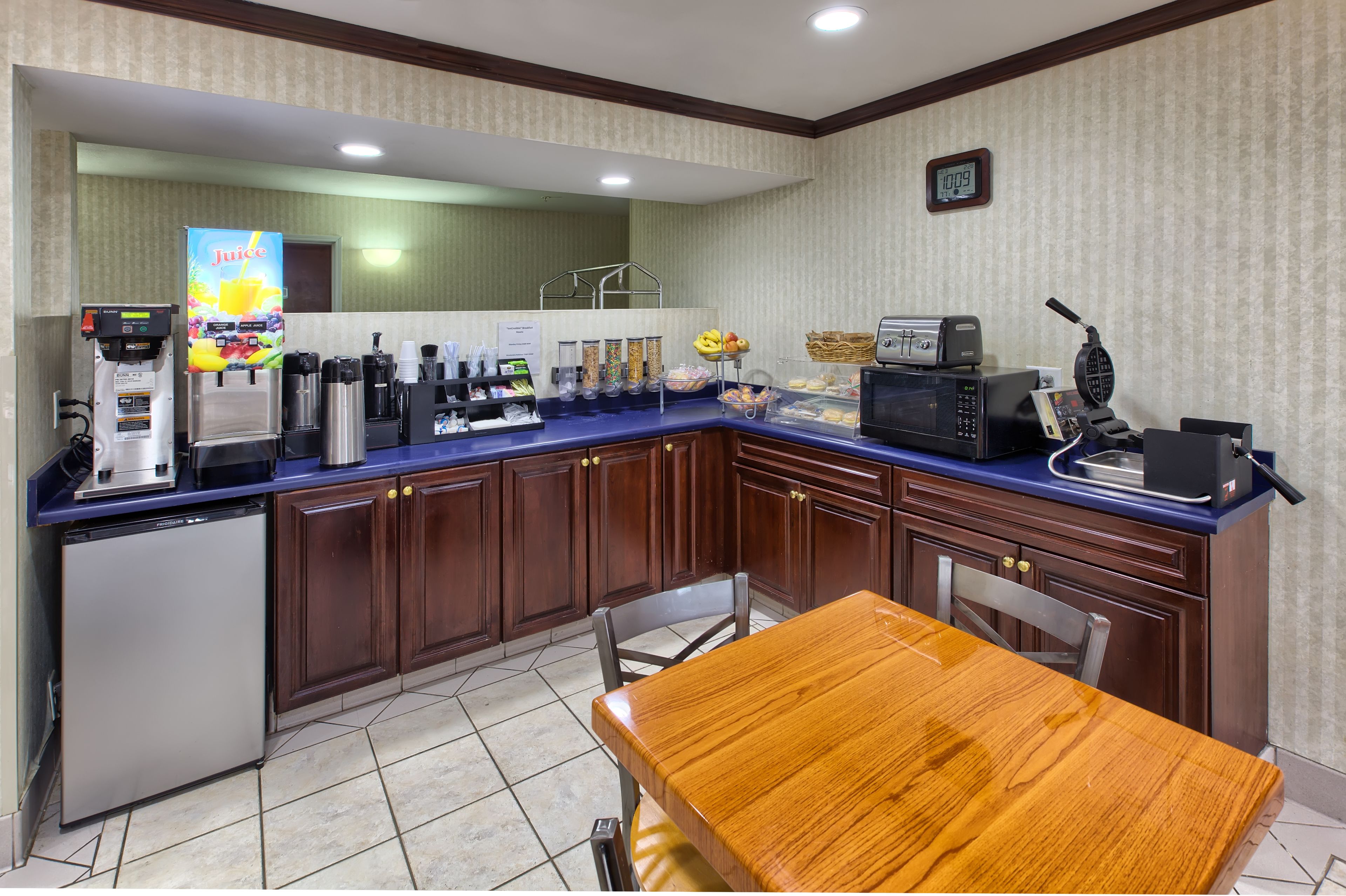 Una kitchenette equipada con refrigerador, cafetera, microondas y tostadora. Incluye una mesa de madera y sillas.