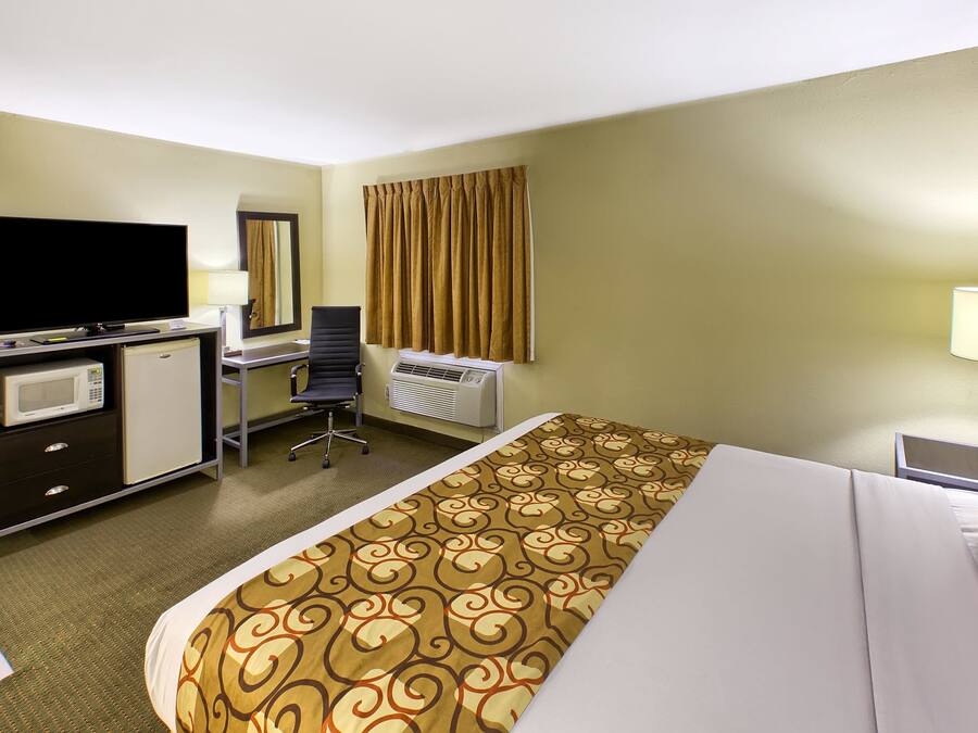 A hotel room with a bed, a desk, a television, a microwave, a chair, and an air conditioning unit.