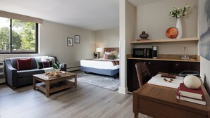 Una sala de estar moderna con un sofá, una mesa de centro y un comedor con una mesa y sillas. Se ve una cama al fondo.