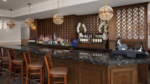 Zona de bar con mostrador de mármol, sillas de madera y una variedad de botellas de licor.