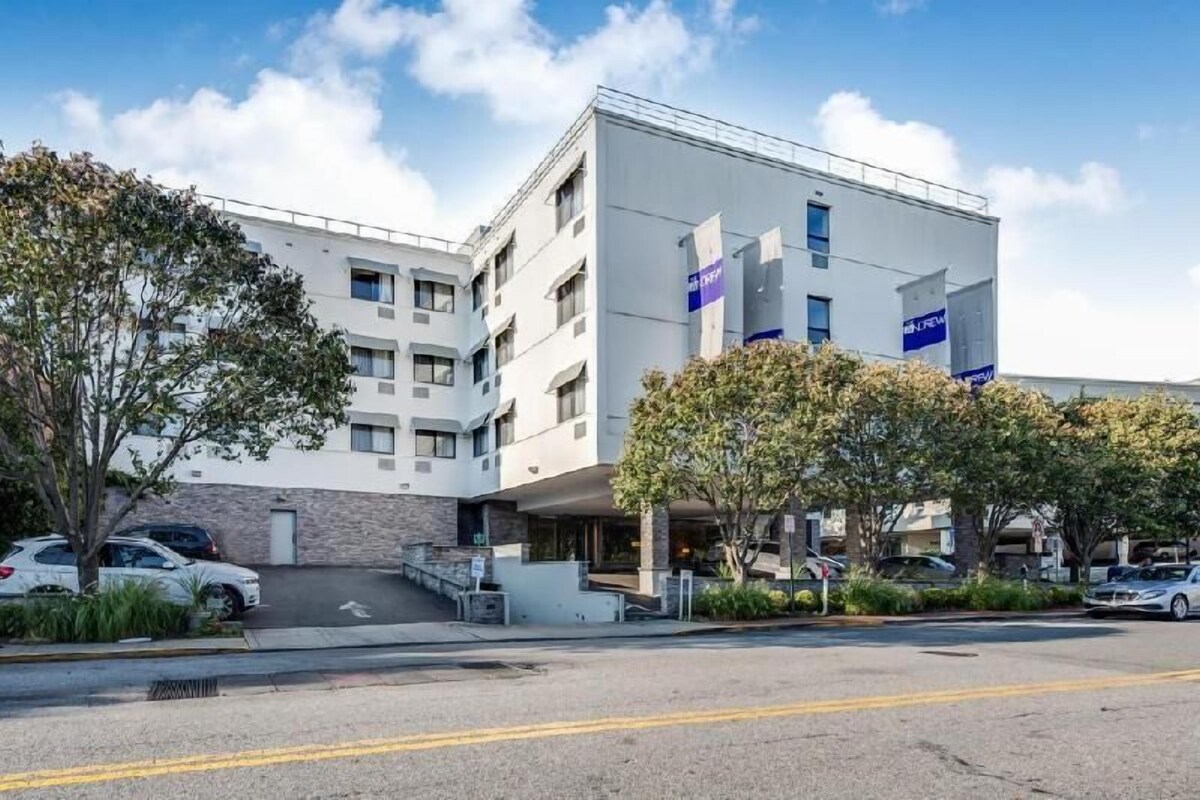 A modern building with a white facade, multiple windows, and a parking lot with cars.